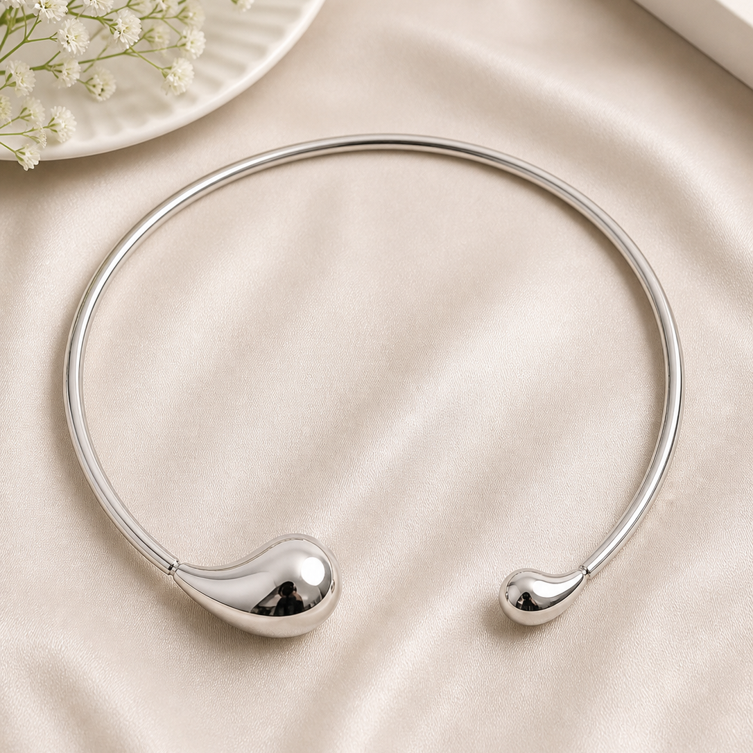Silver necklace on a beige surface with a small plate of flowers in the background