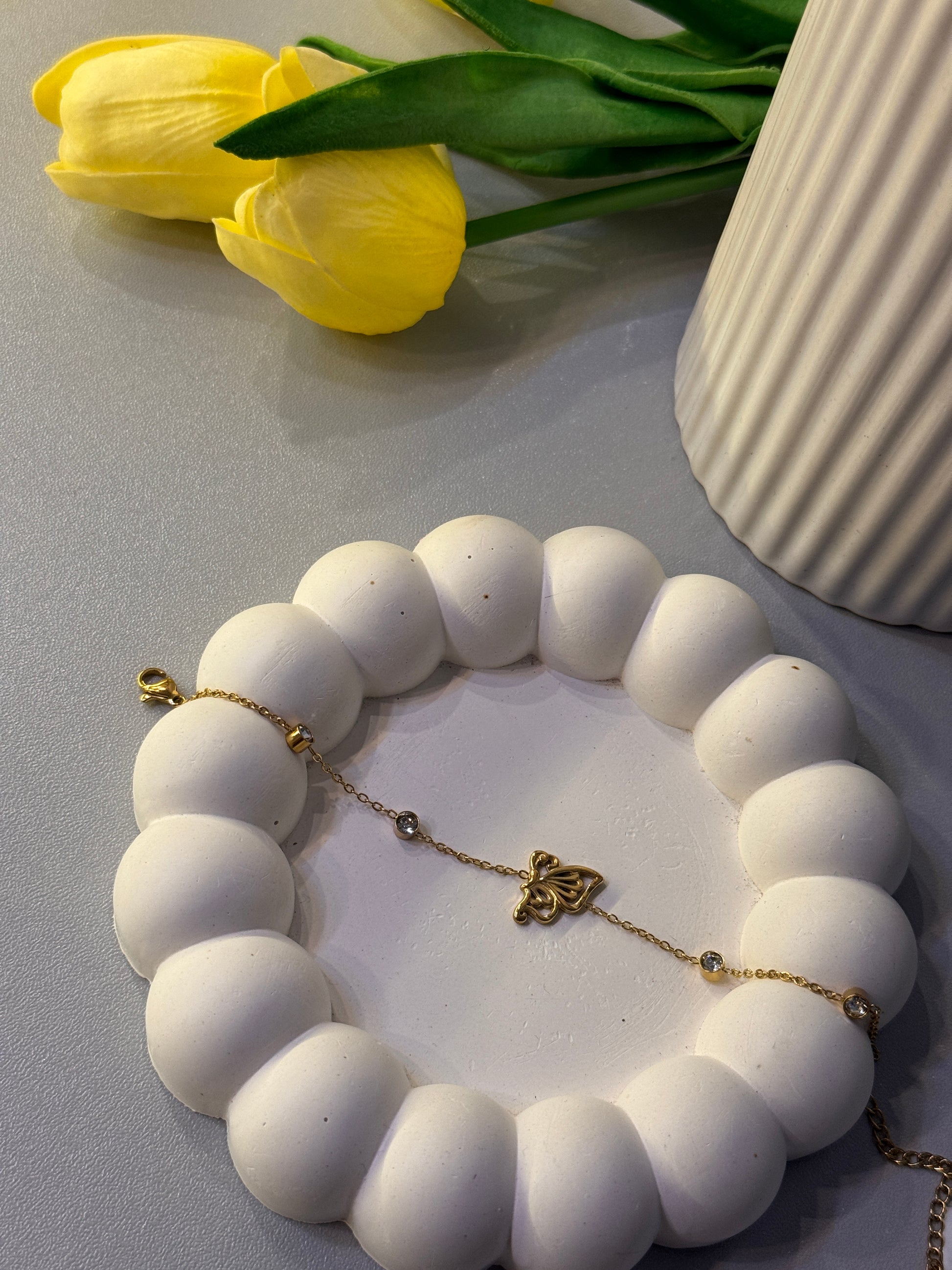White beaded bracelet with gold accents on a white surface next to yellow tulips.