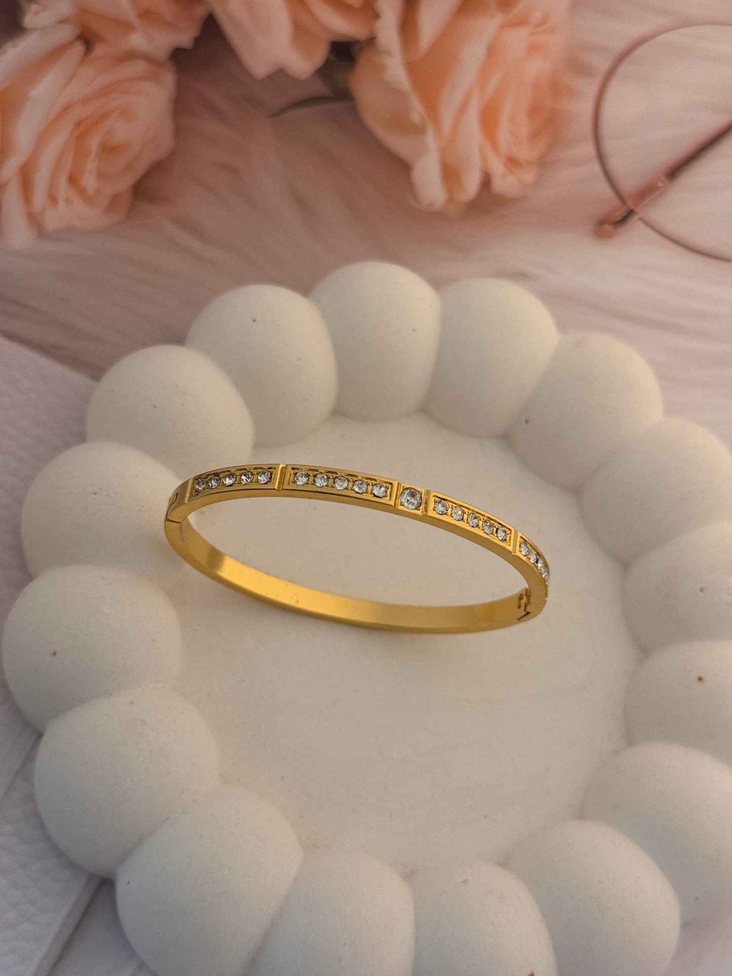 Gold ring with small diamonds on a white textured surface with pink flowers.