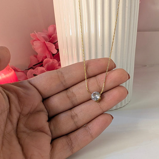 Gold necklace with a heart pendant held in a hand against a blurred background