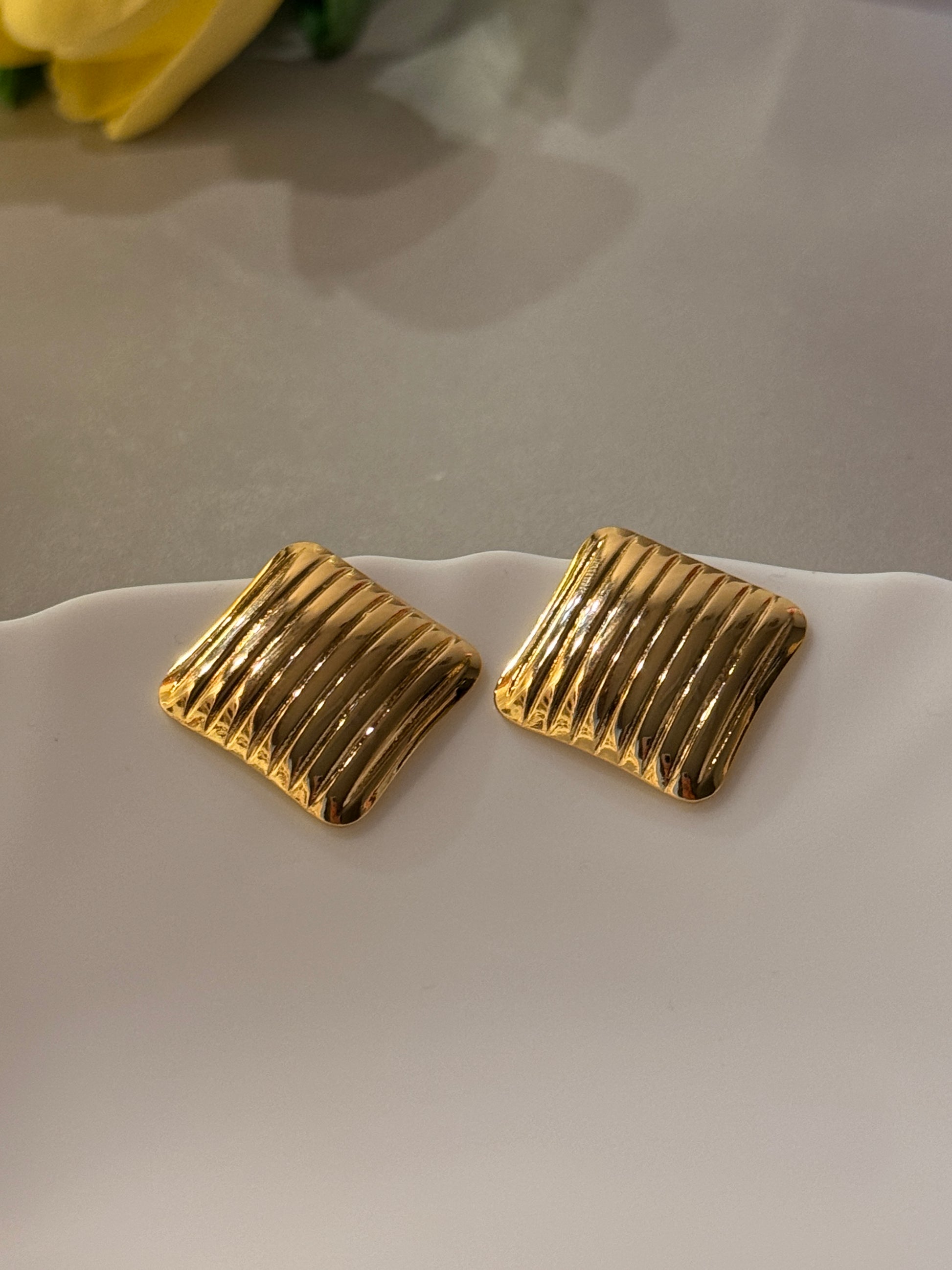 Gold square earrings on a white surface with a blurred background