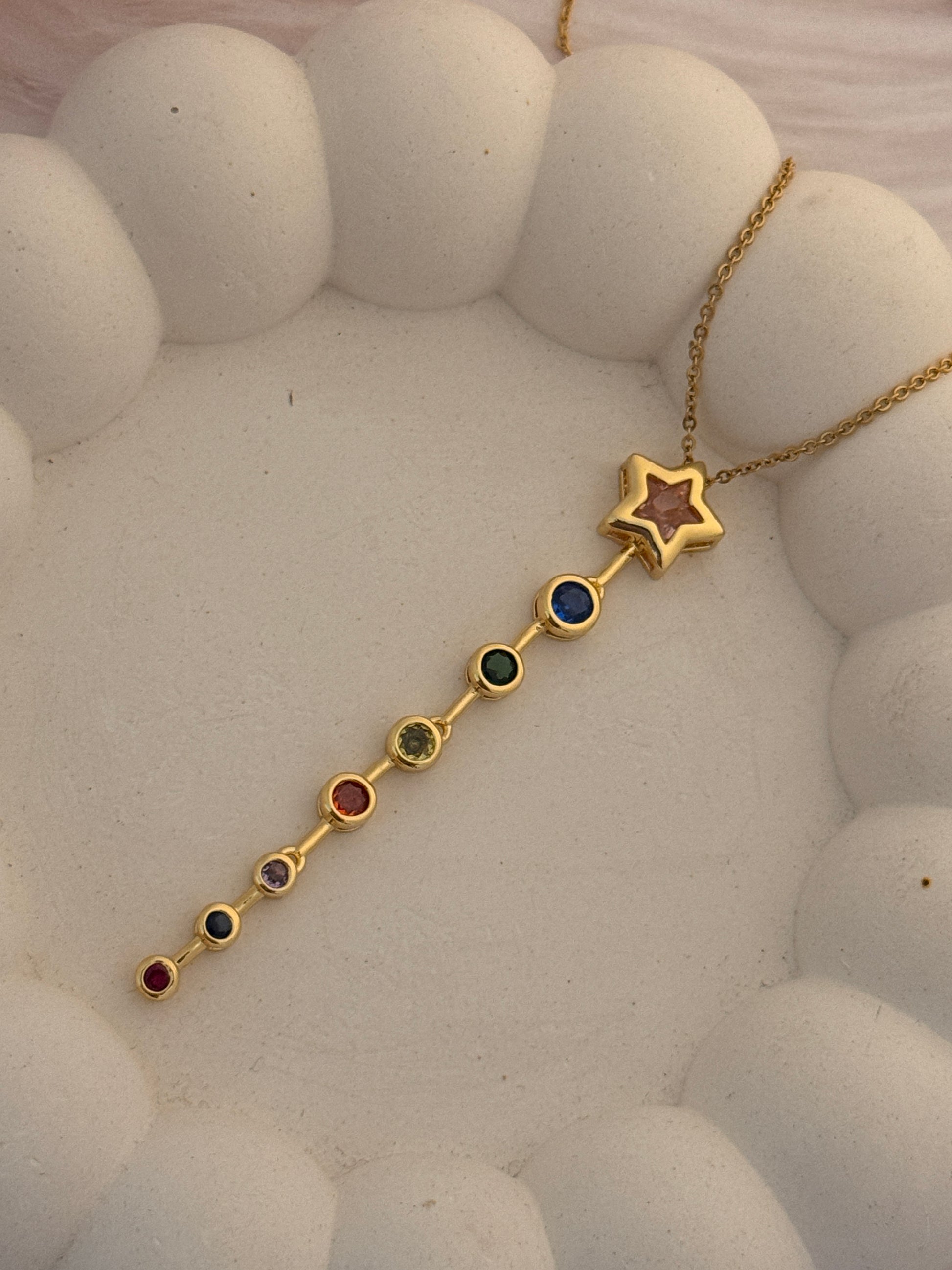 Gold necklace with star and colored gemstones on a textured white surface