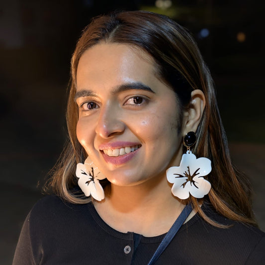 Woman wearing large white earrings with floral designs against a dark background