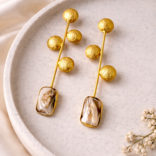 Gold earrings with pearl-like stones on a textured plate with flowers.