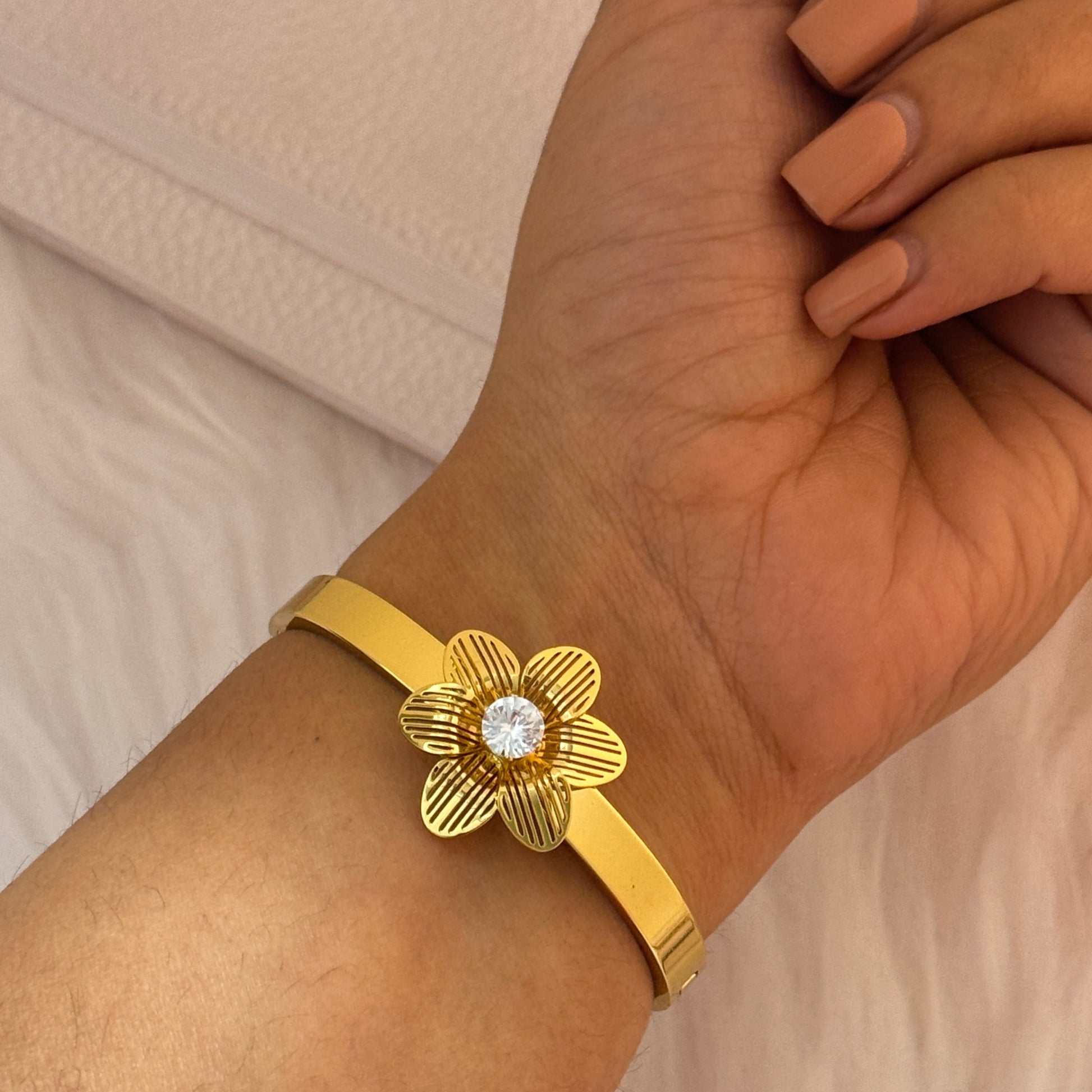 Gold bracelet with a floral design worn on a wrist against a neutral background