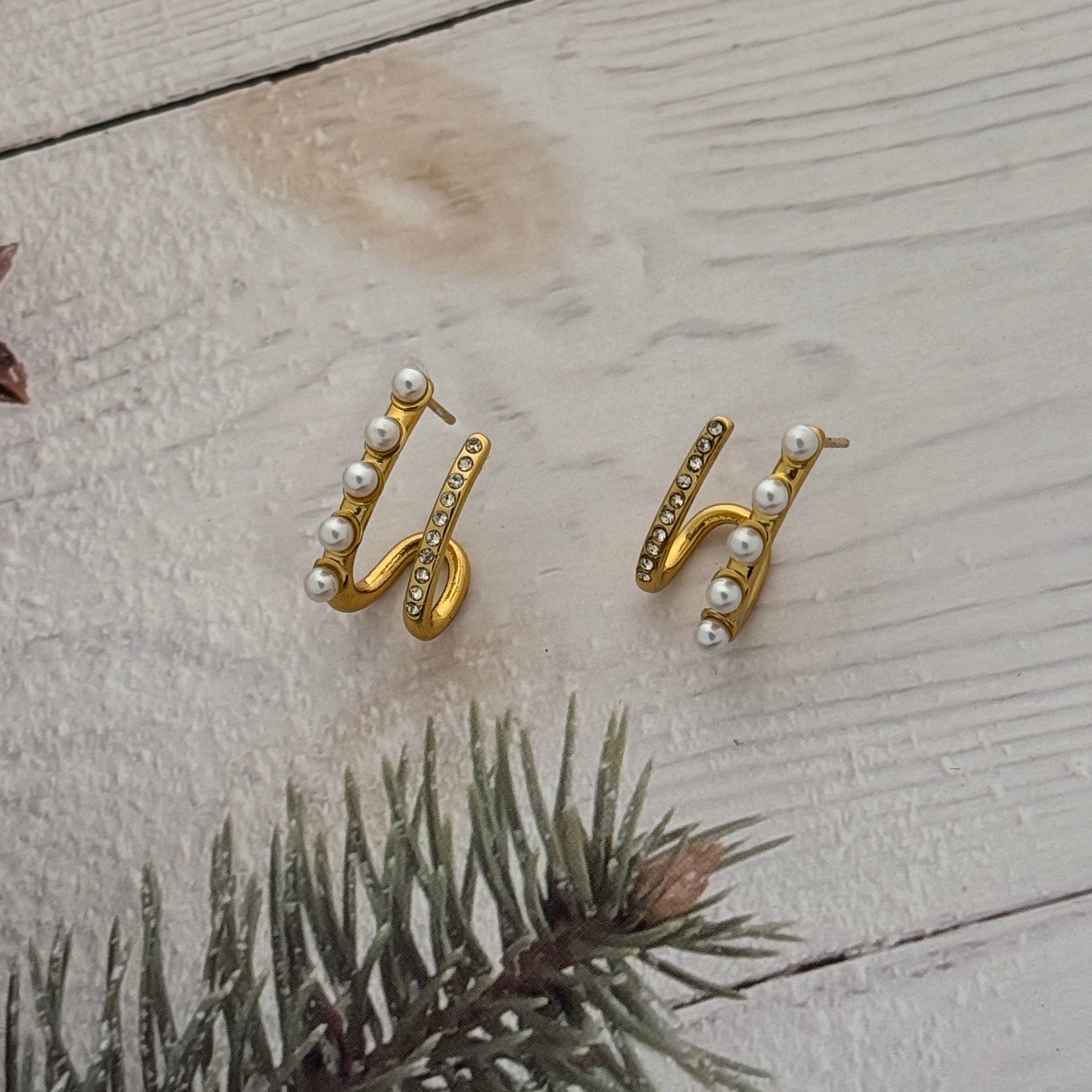 Gold earrings with pearl accents on a textured surface with a branch.