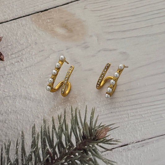 Gold earrings with pearl accents on a textured surface with a branch.