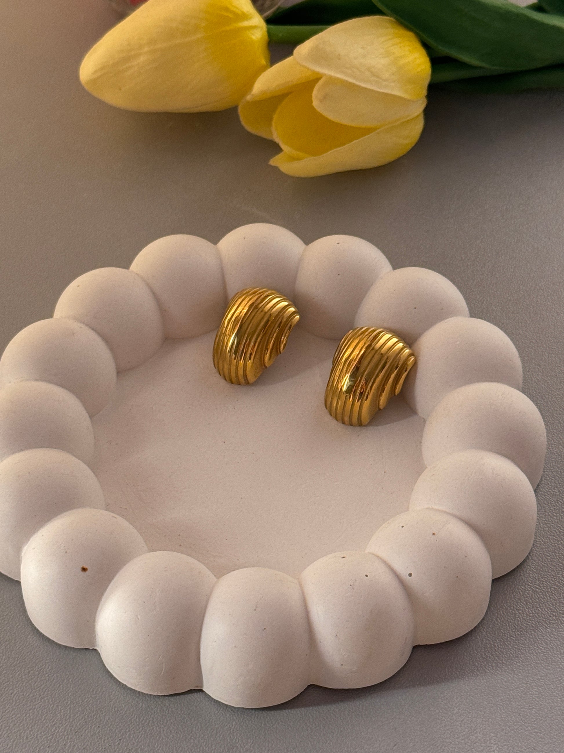 Gold earrings on a white stone surface with yellow tulips on the side