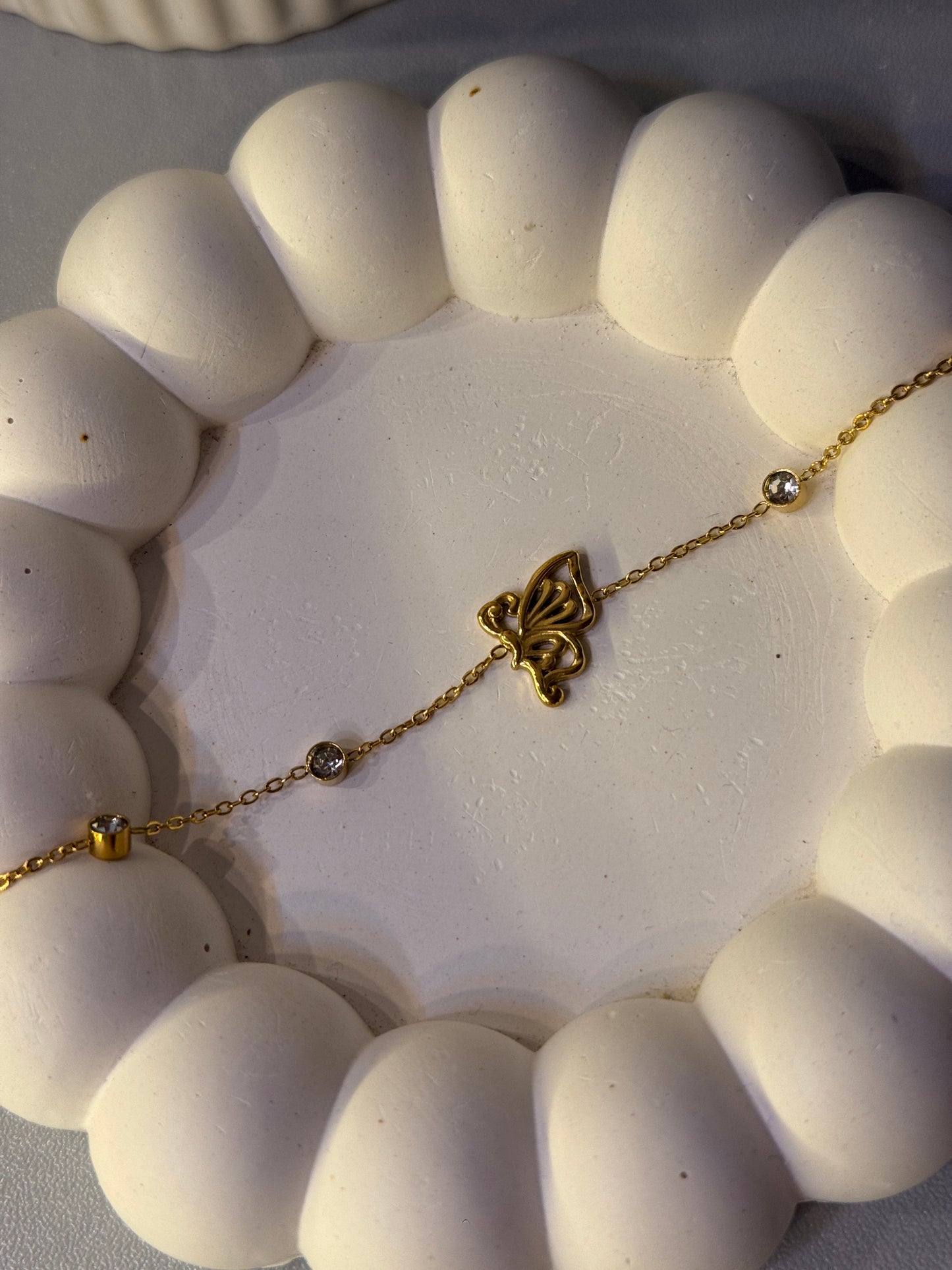 Close-up of a white beaded bracelet with a gold chain and clasp on a light gray background.