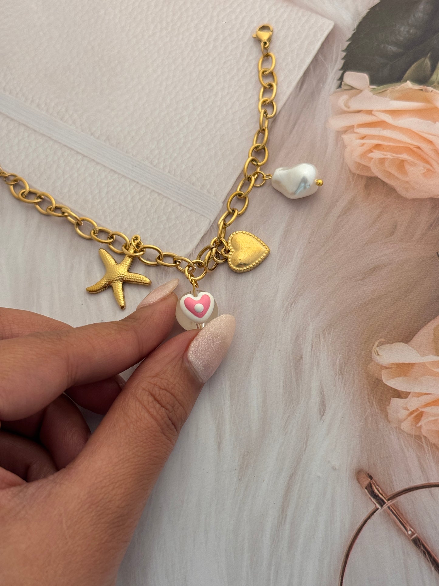 Gold bracelet with heart and starfish charms held by a hand on a light background
