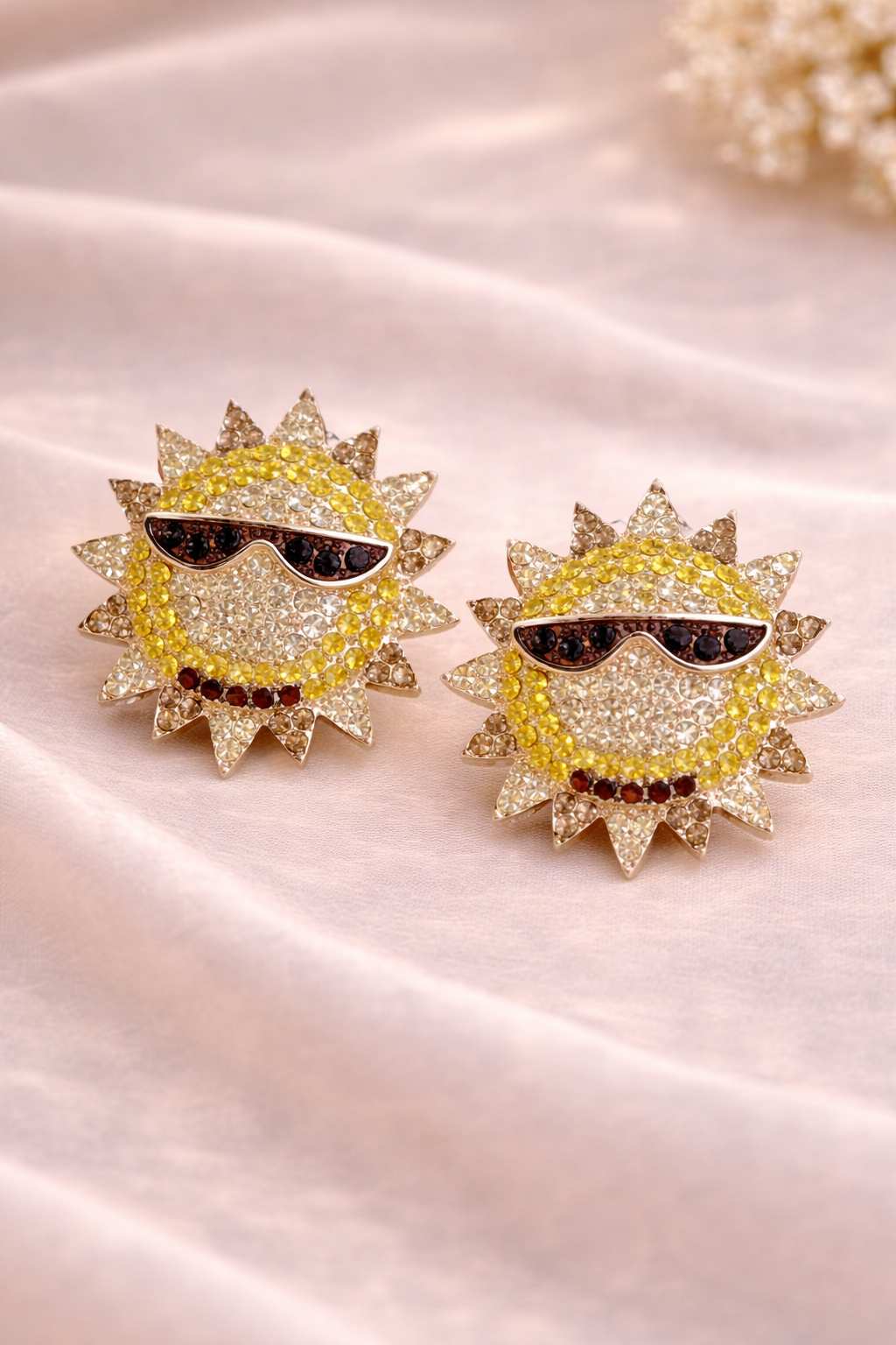 Sun-shaped earrings with sunglasses design on a satin surface