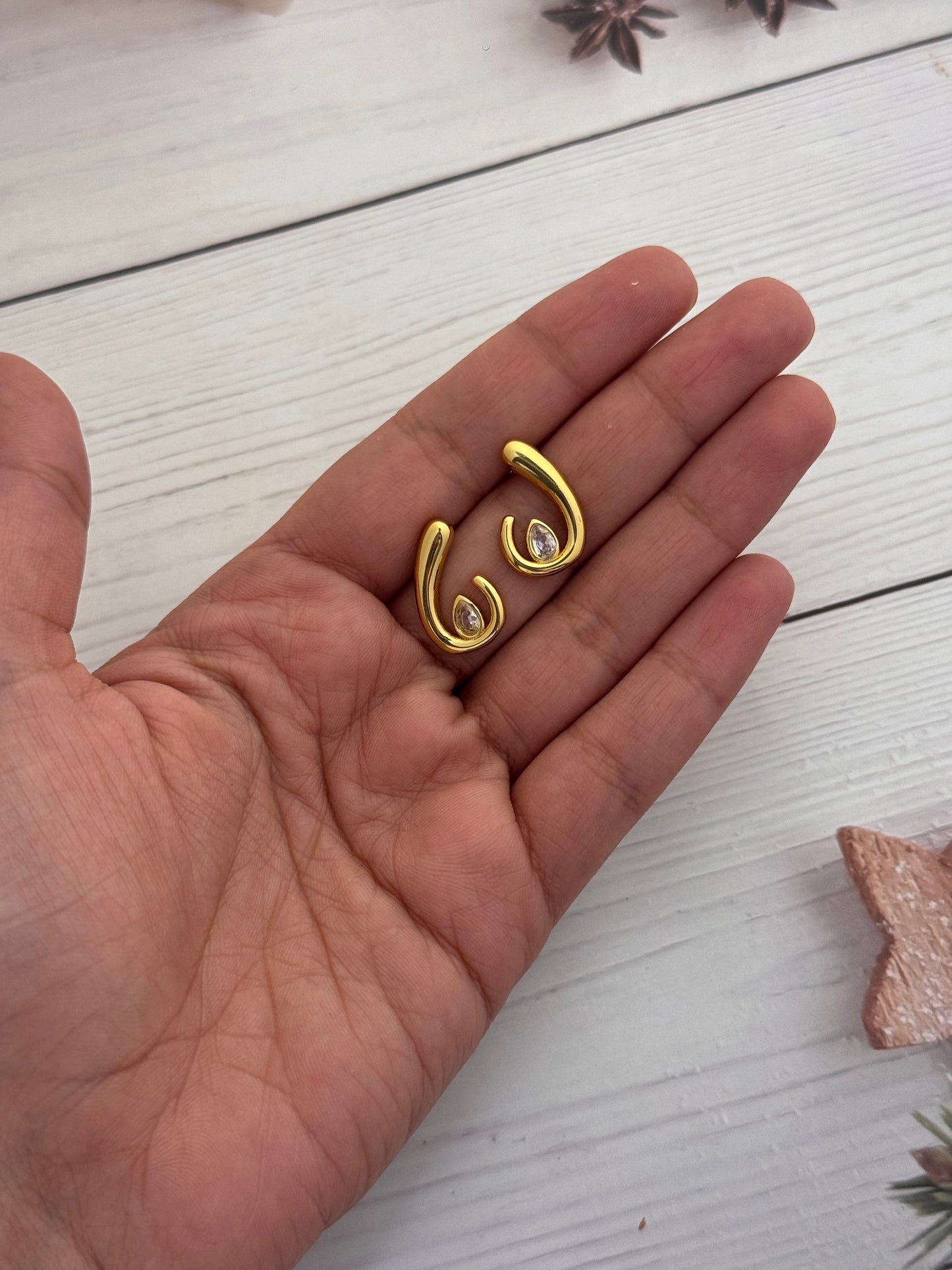 Gold earrings held in a hand on a light wooden surface