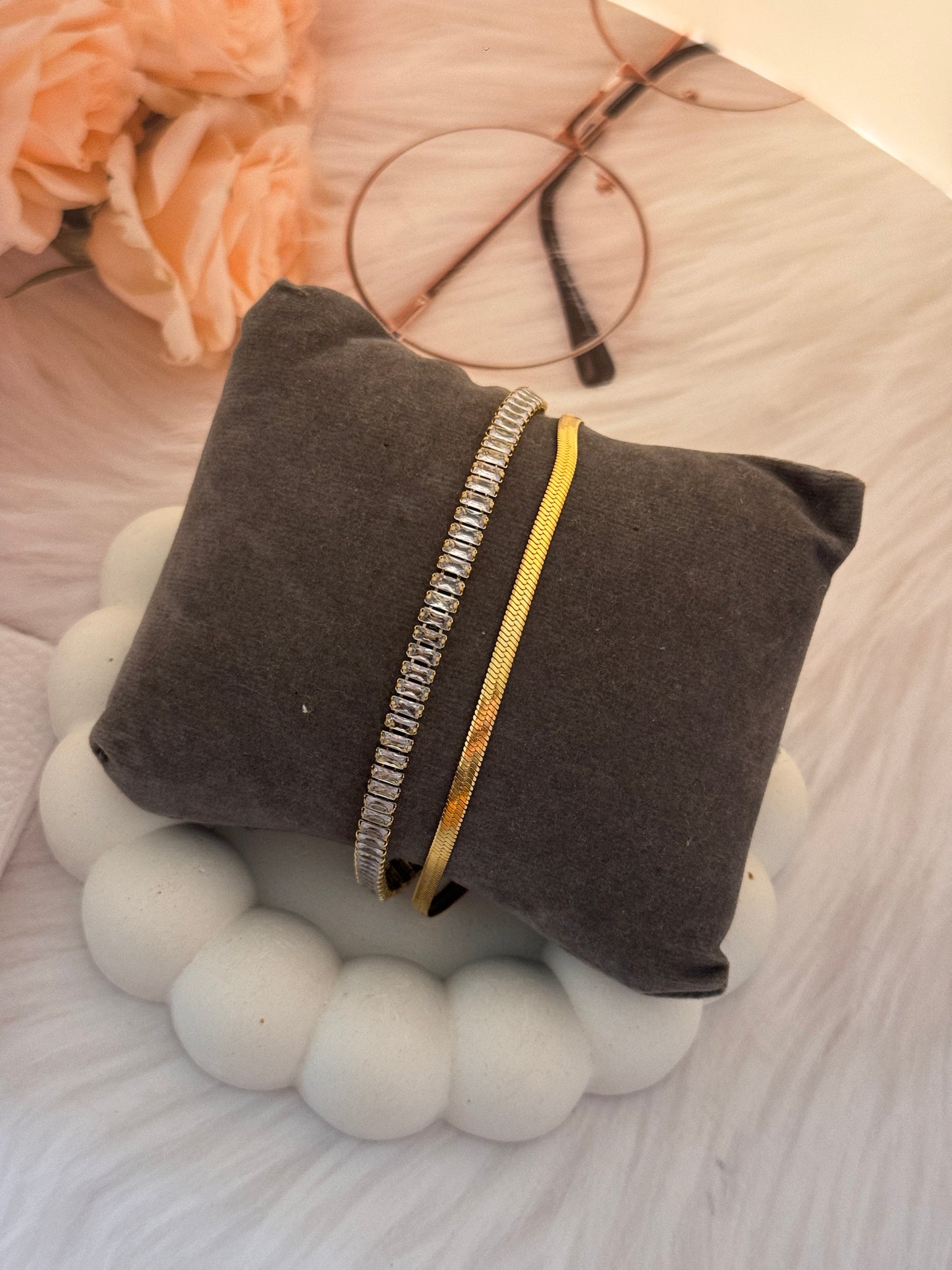 Gray pillow with decorative band on a textured surface with flowers and glasses in the background