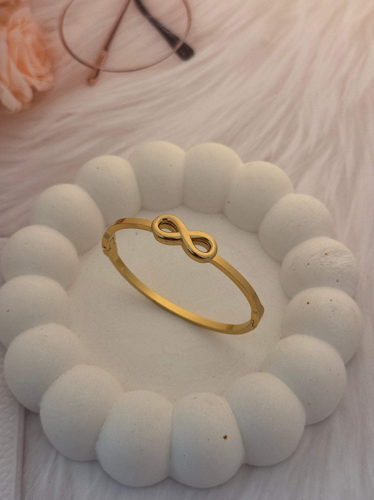 Gold infinity ring on a white beaded bracelet with a blurred background