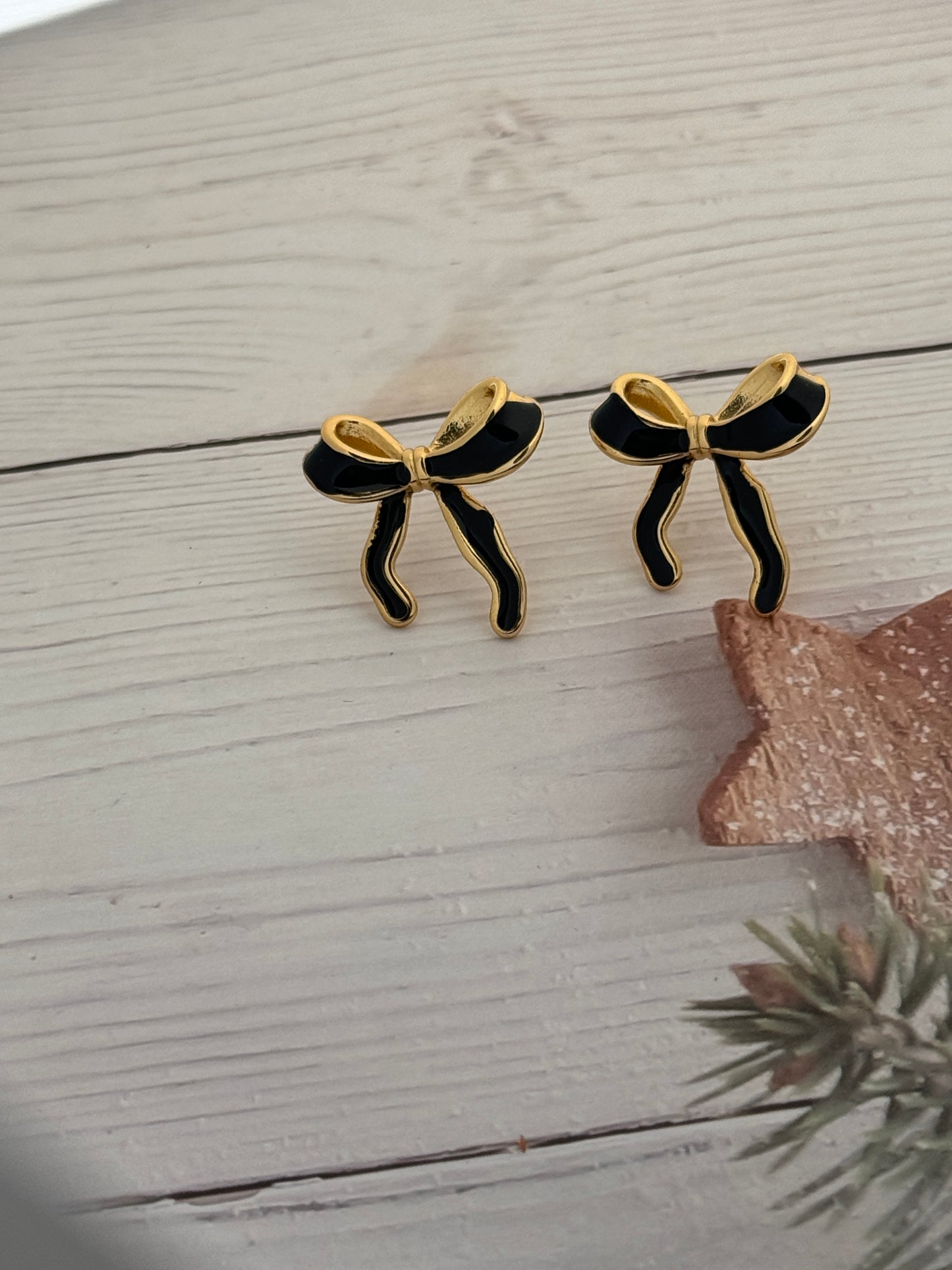 Black and gold butterfly earrings on a light wooden surface with a decorative star and plant.