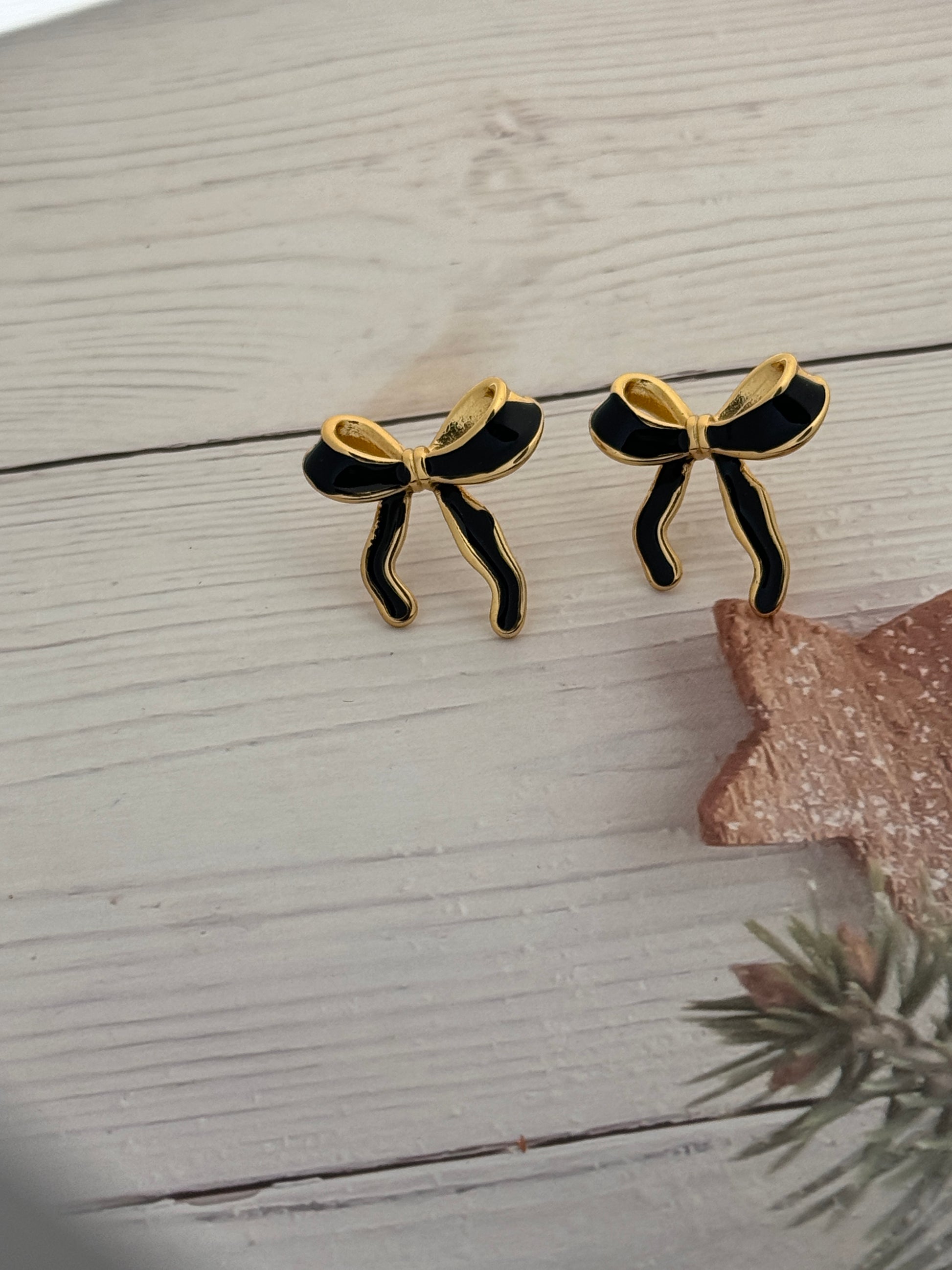 Black and gold butterfly earrings on a light wooden surface with a decorative star and plant.