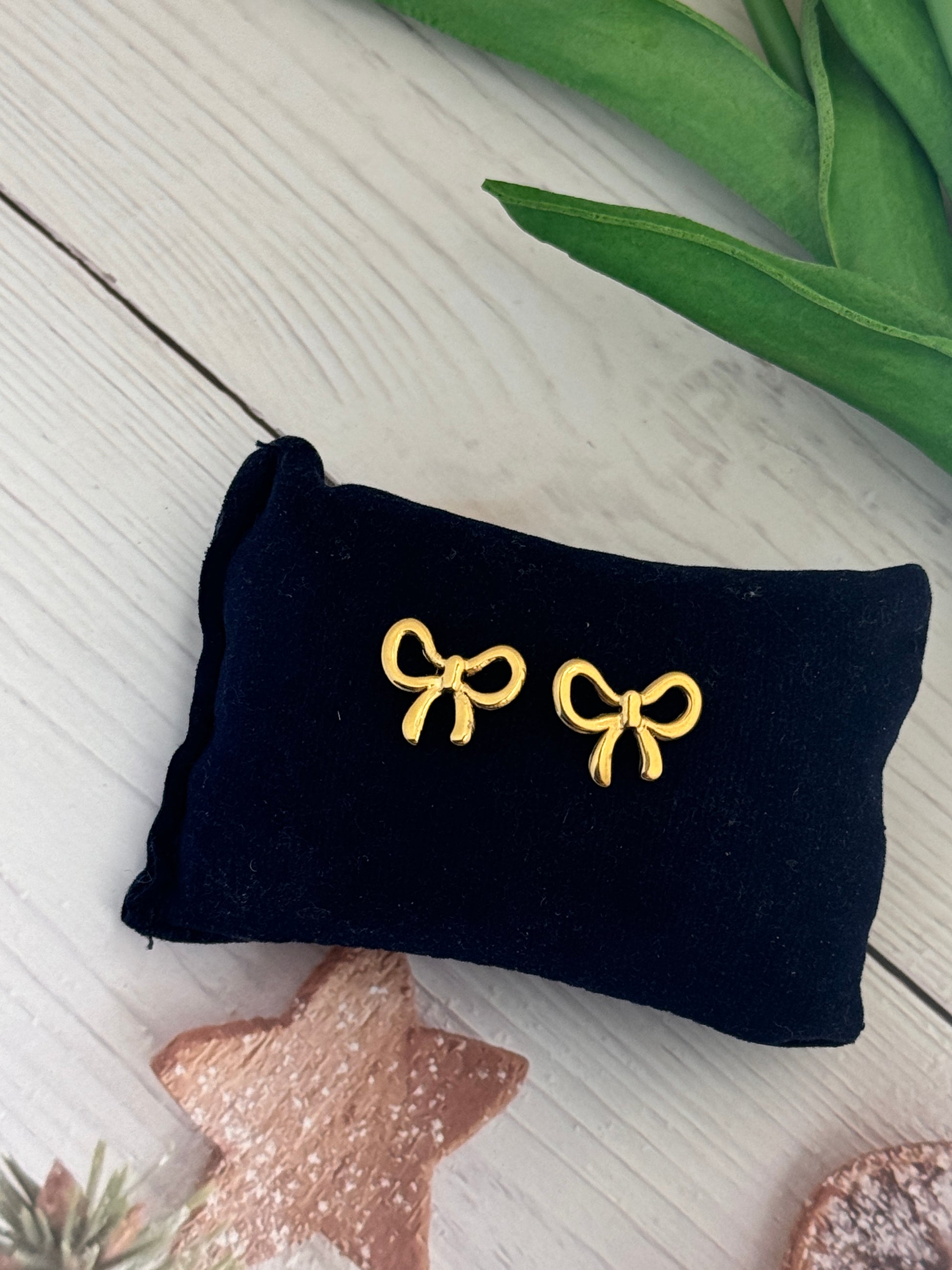 Black velvet jewelry pouch with gold bow-shaped earrings on a light wooden surface.