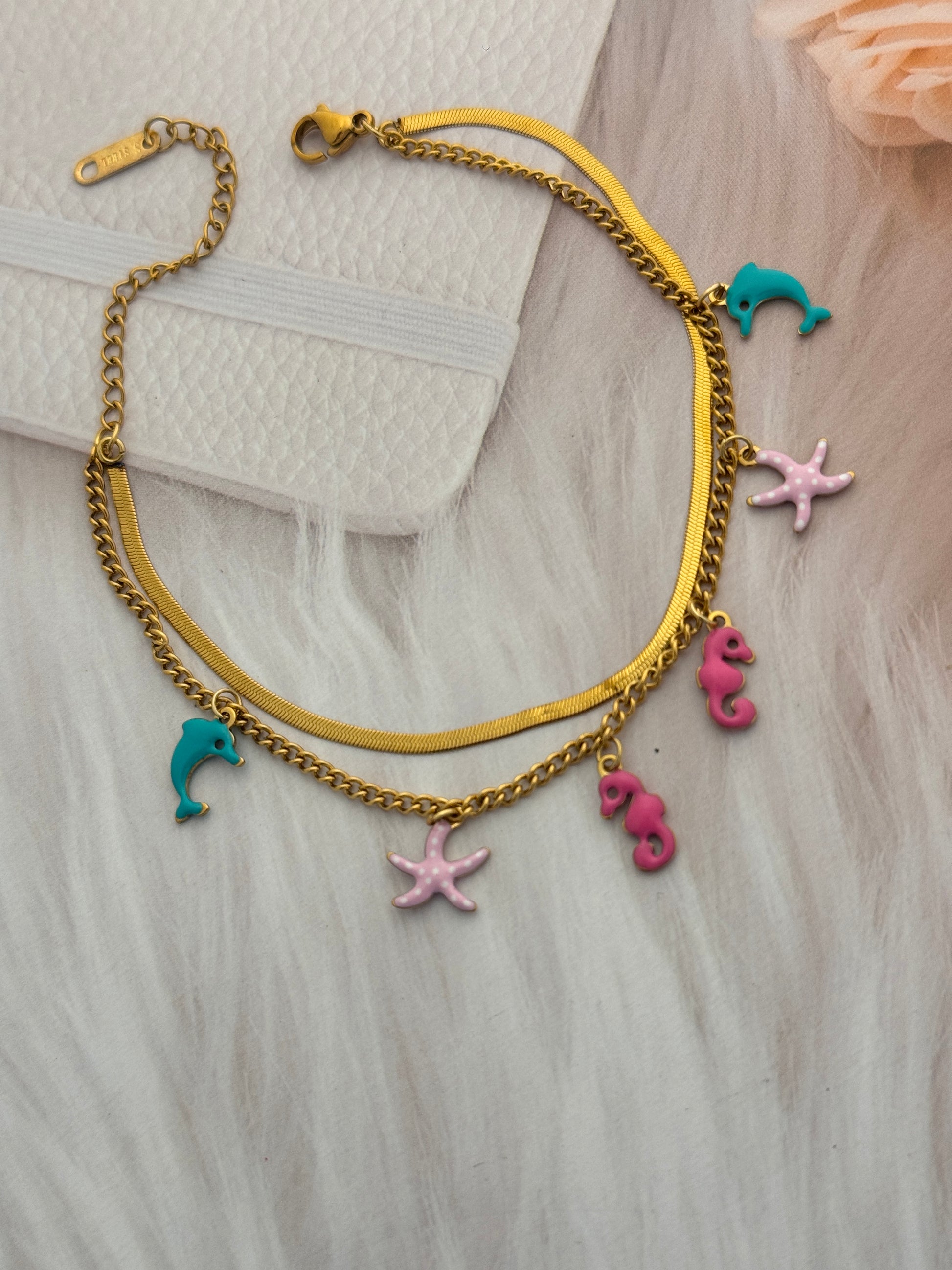 Gold bracelet with colorful charms on a textured surface
