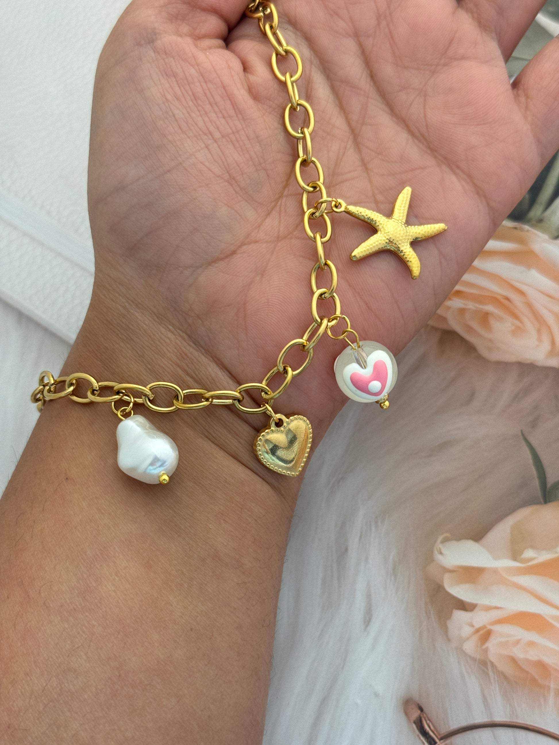 Gold bracelet with starfish, heart, and bird charms on a wrist.