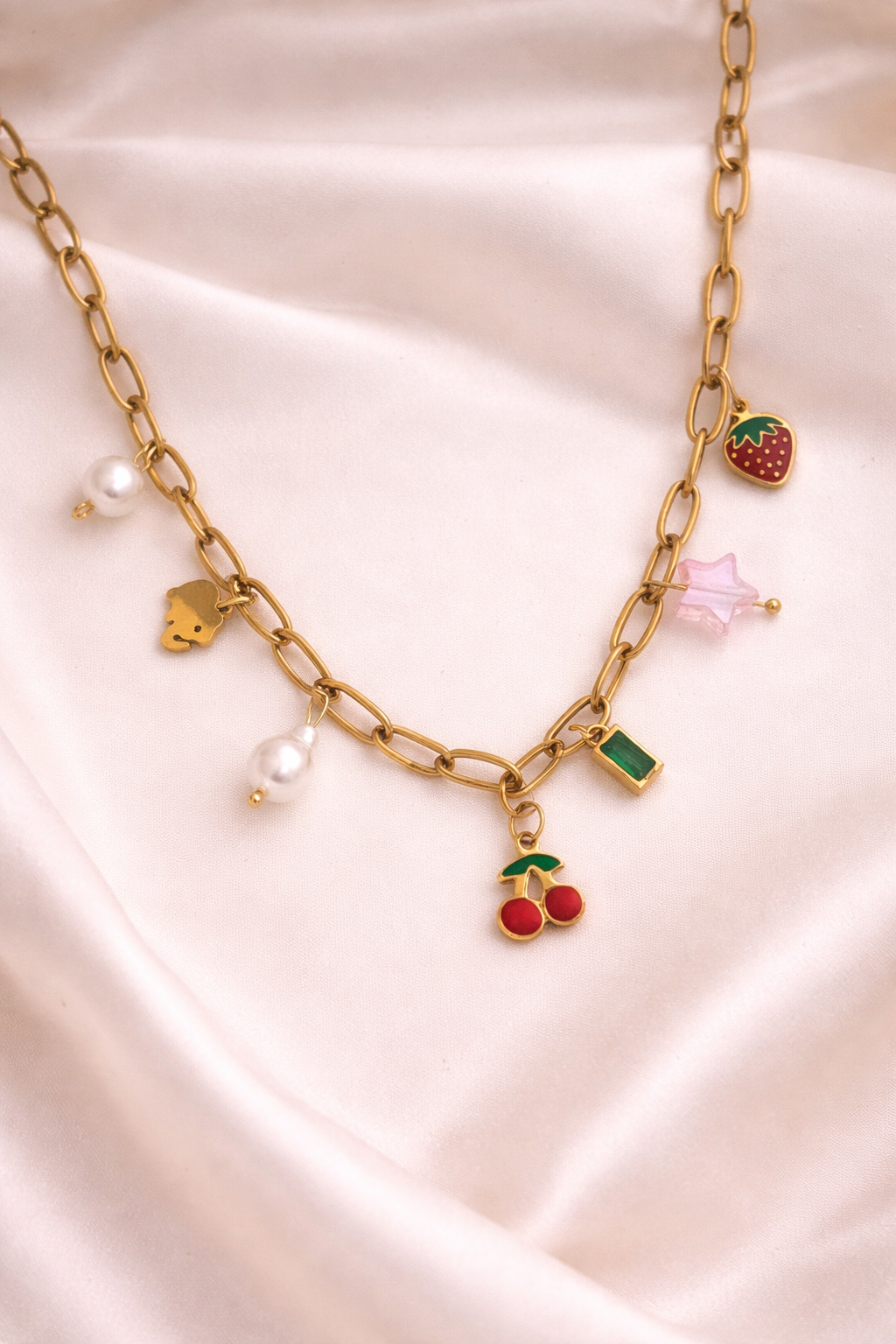 Gold chain necklace with various charms on a pink satin background