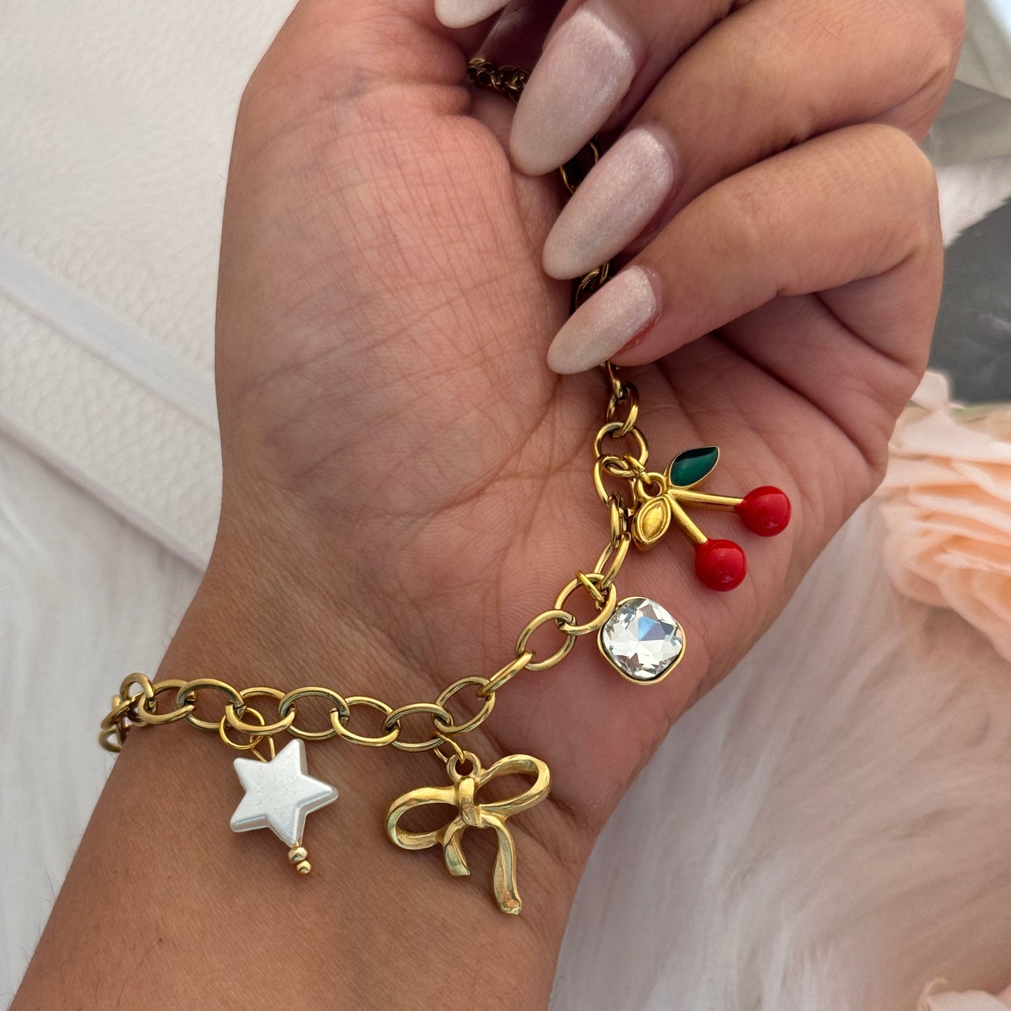 Gold bracelet with charms on a wrist against a neutral background