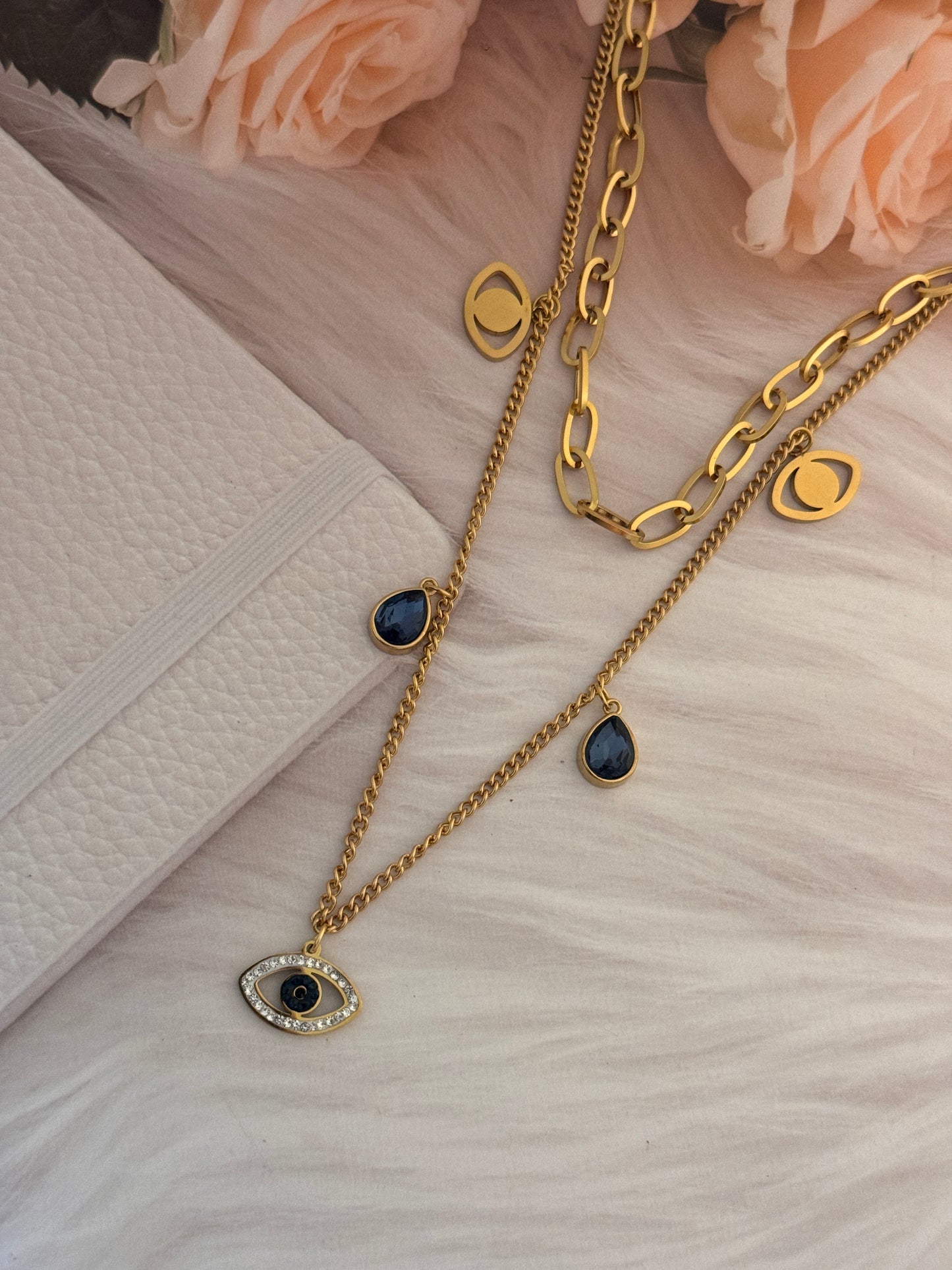 Gold necklaces with gemstones on a textured surface with flowers
