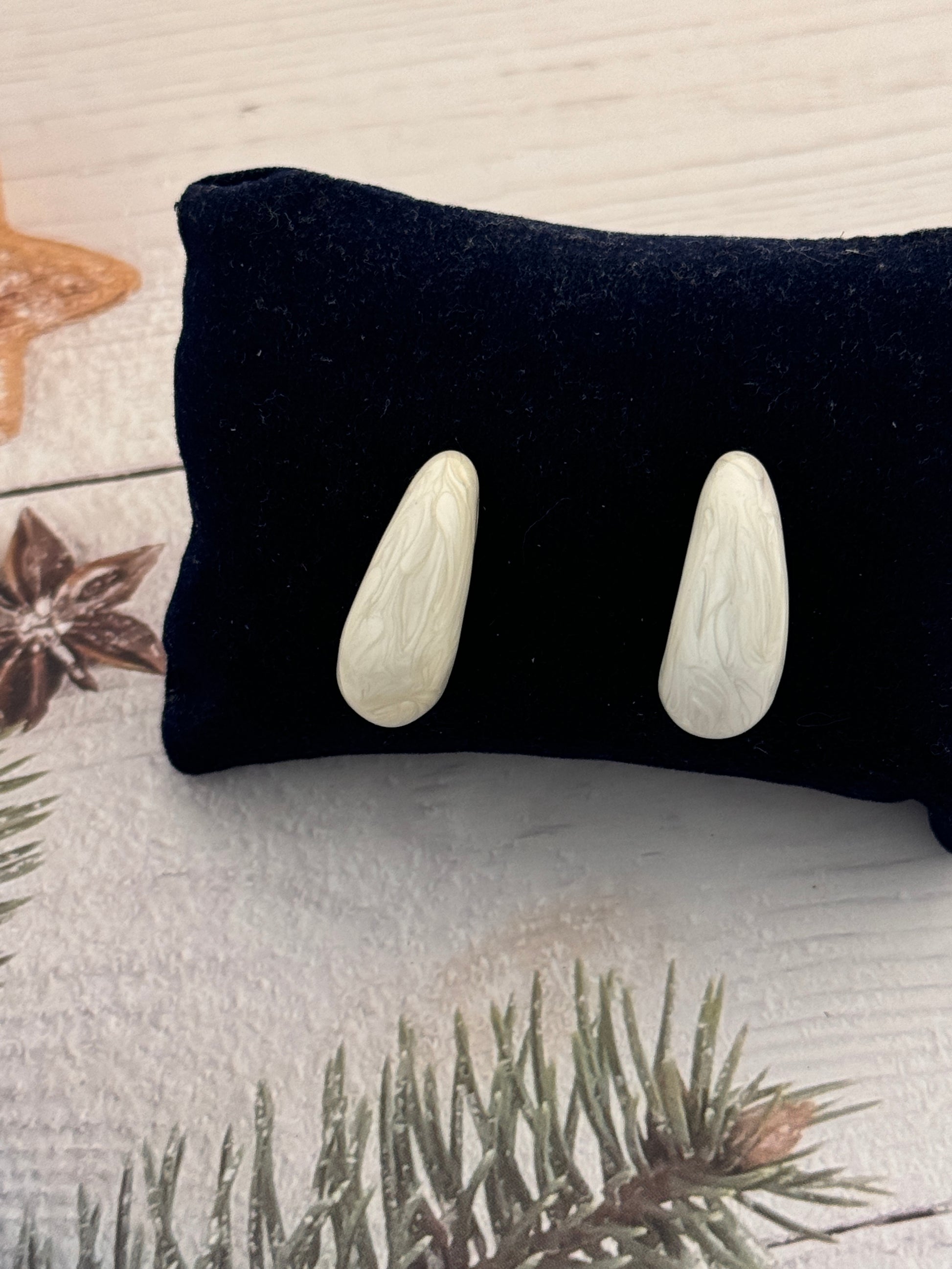Black pillow with three white stones on a textured surface with greenery