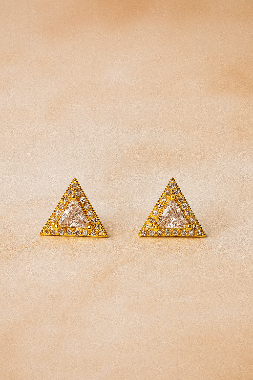 Triangle-shaped earrings with clear gemstones and gold accents on a beige background