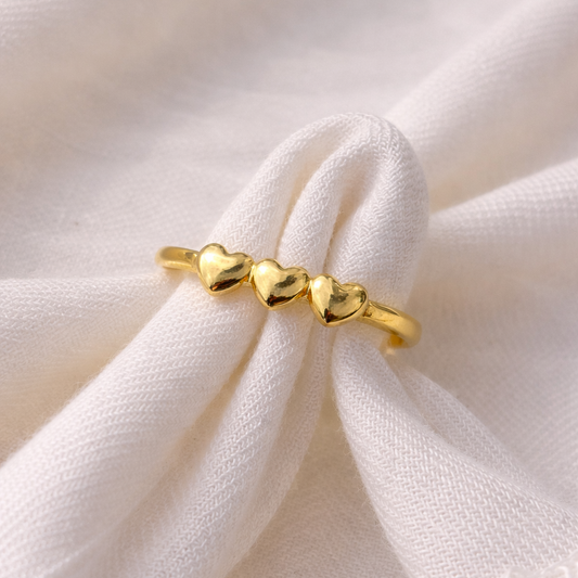 Gold ring with heart-shaped beads on a white fabric background