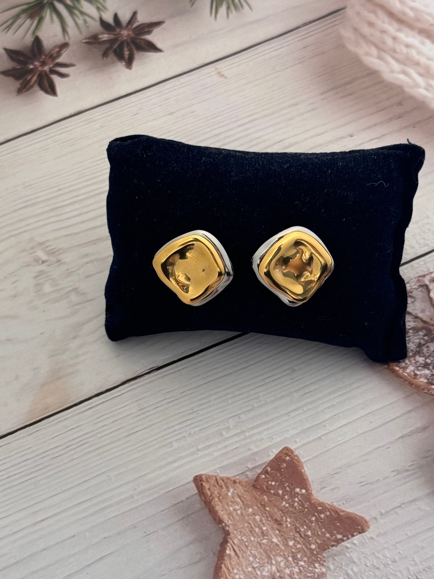 Gold earrings on a black cushion with a star-shaped object and pine branches in the background.