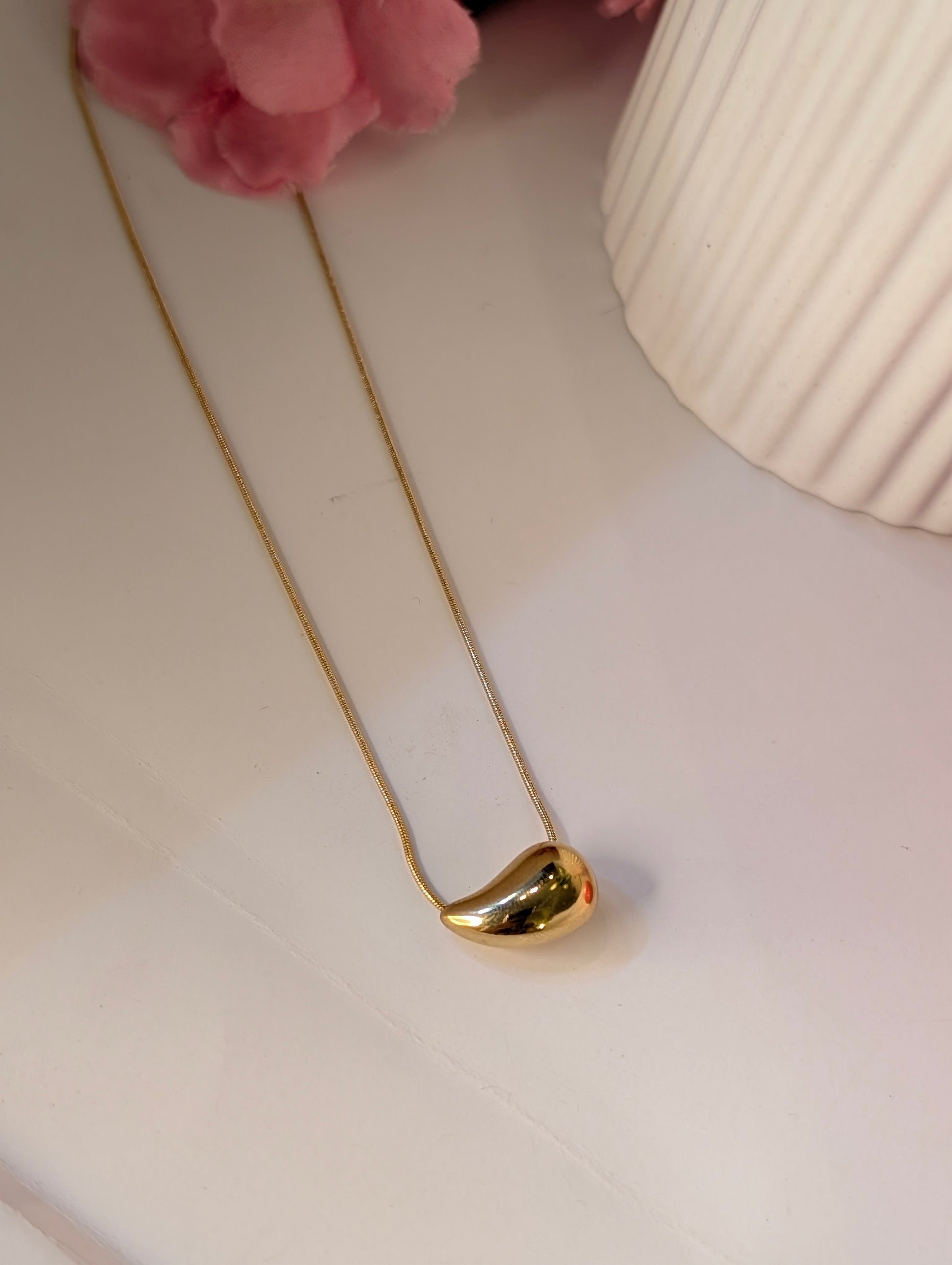 Gold necklace on a white surface with a pink flower in the background