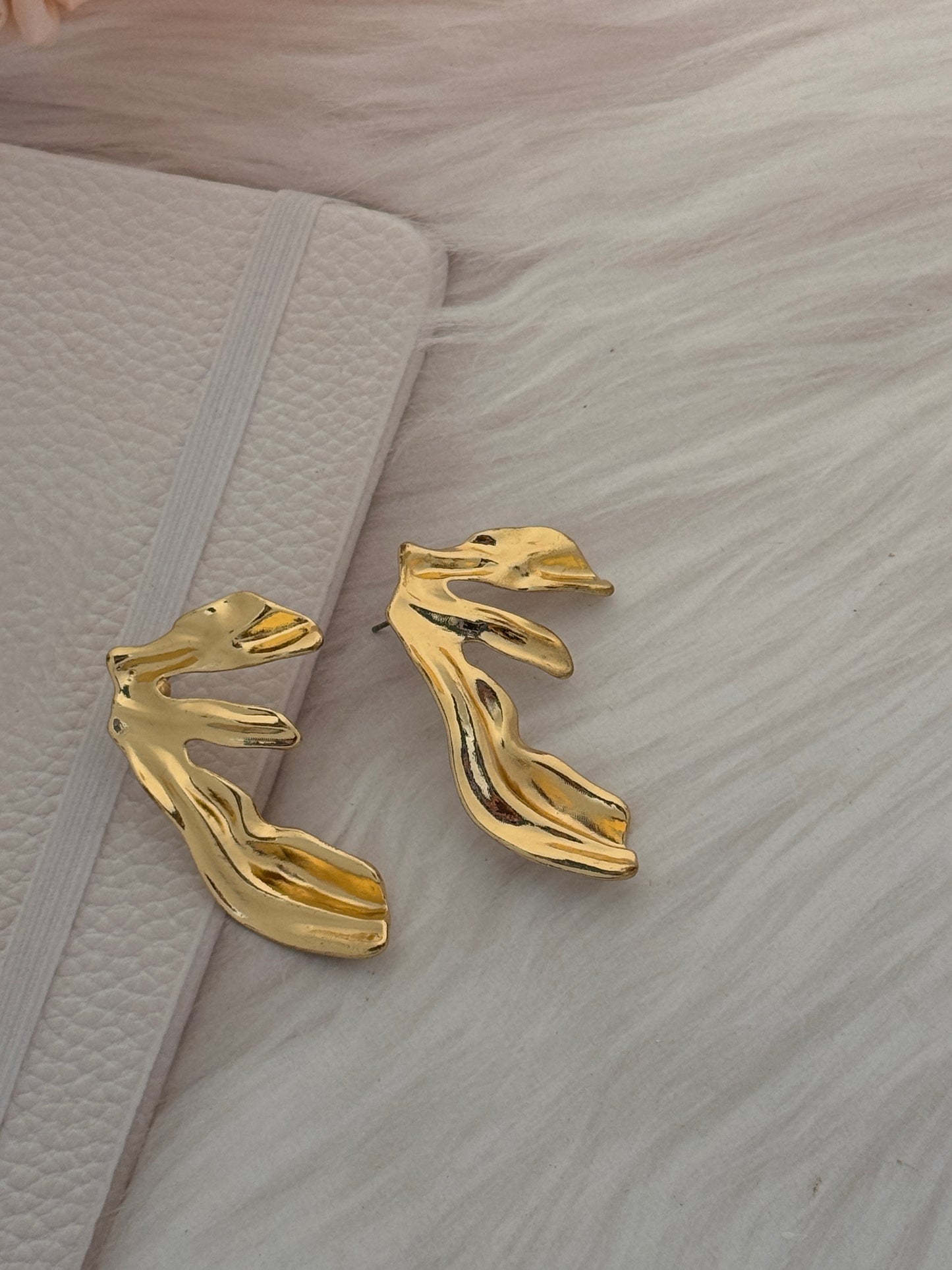 Gold deer-shaped earrings on a textured surface