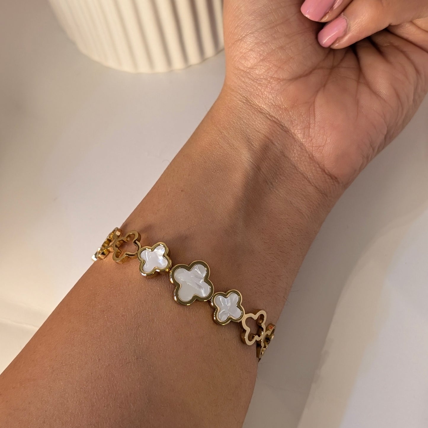 Gold bracelet with white flower-shaped charms on a wrist against a neutral background