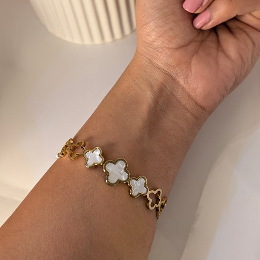 Gold bracelet with white flower-shaped charms on a wrist against a neutral background
