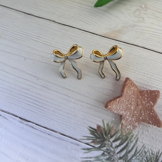 Pair of bow-shaped earrings on a wooden surface with a yellow tulip and decorative star.