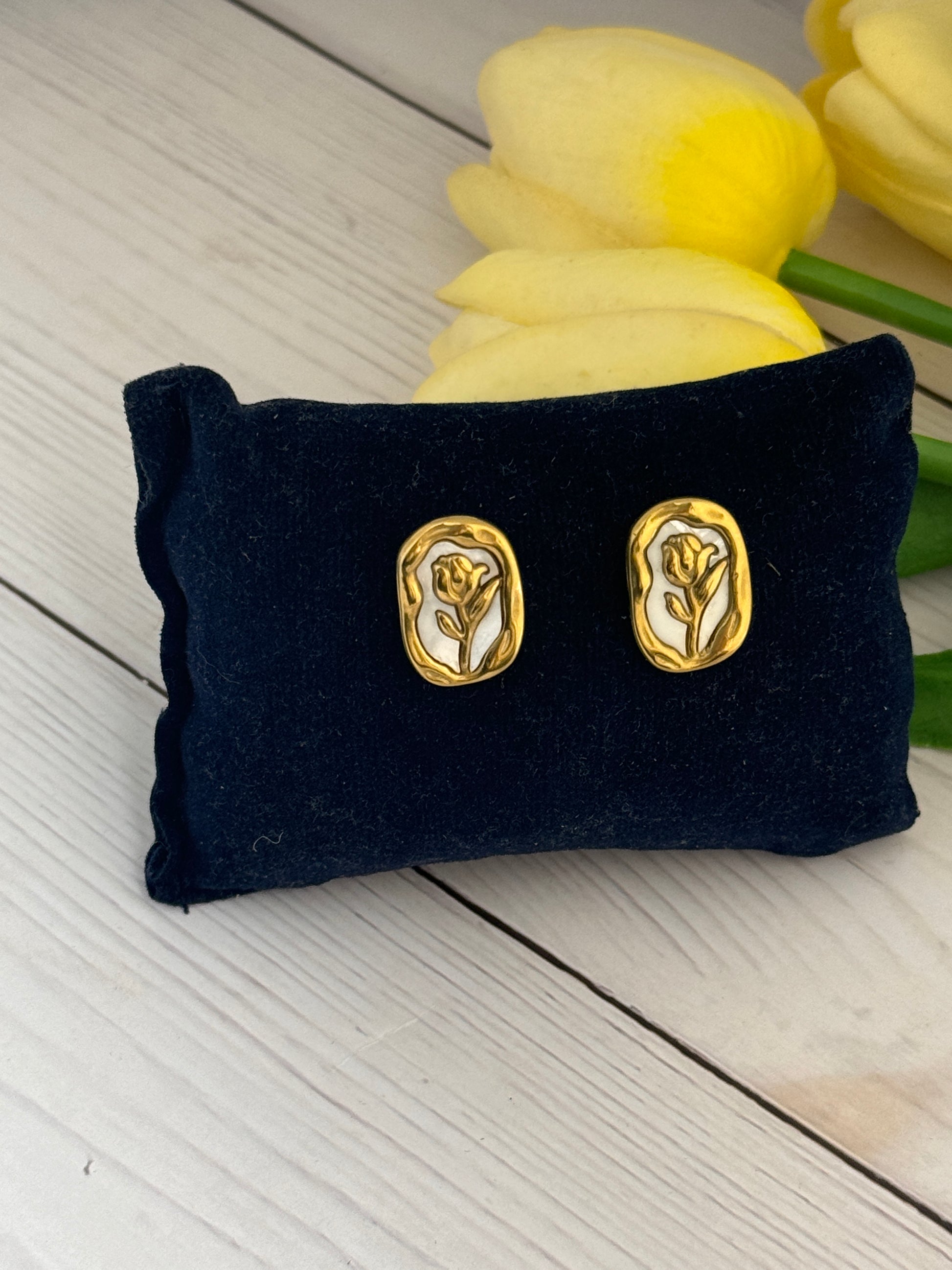Gold earrings on a black pillow with yellow tulips in the background