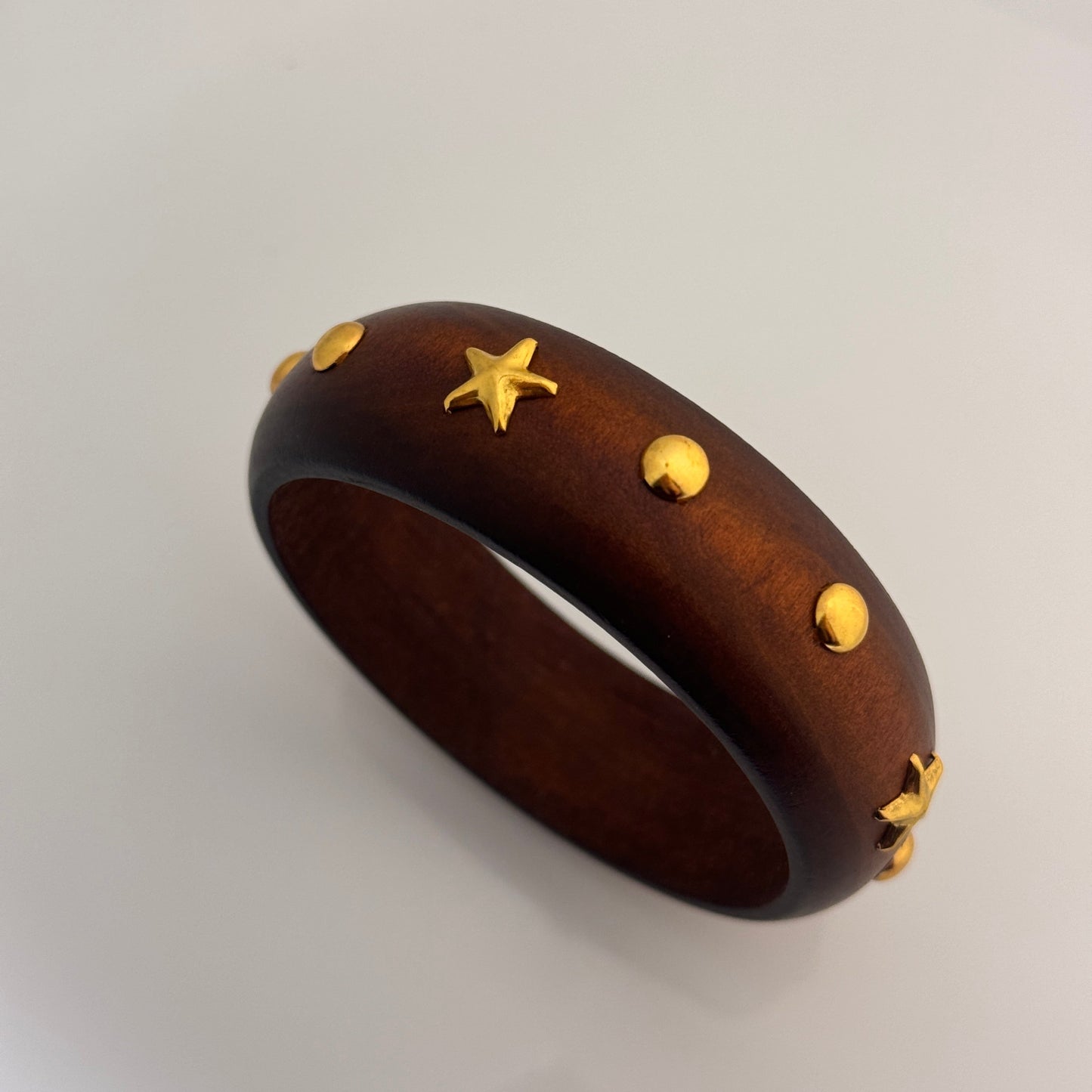 Wooden bracelet with gold star and circle accents on a light gray background