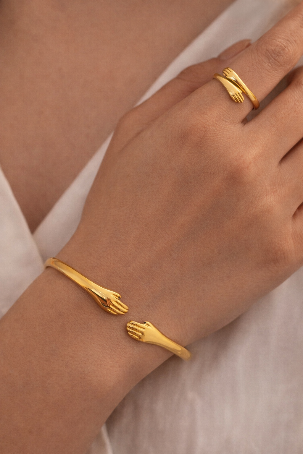 Gold bracelet and ring on a person's wrist against a neutral background