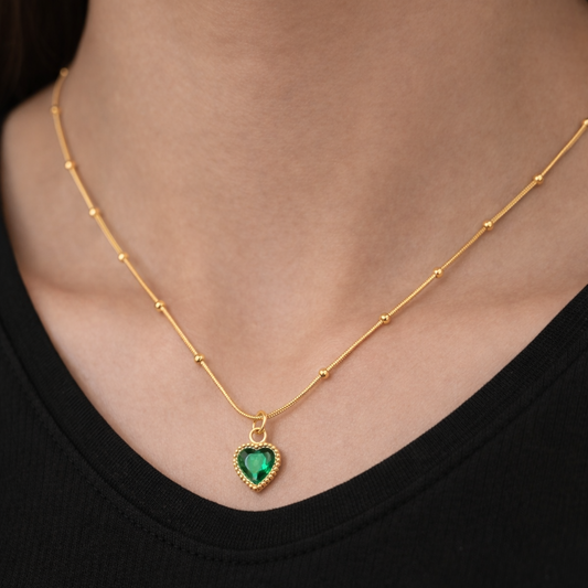Gold necklace with a heart-shaped green gemstone pendant on a black background