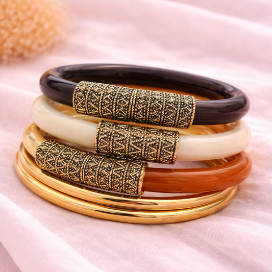 Set of colorful bangles with gold and black patterns on a soft pink fabric background