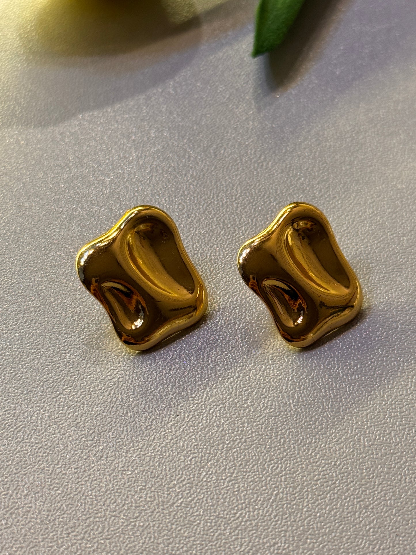 Two gold earrings on a light gray surface