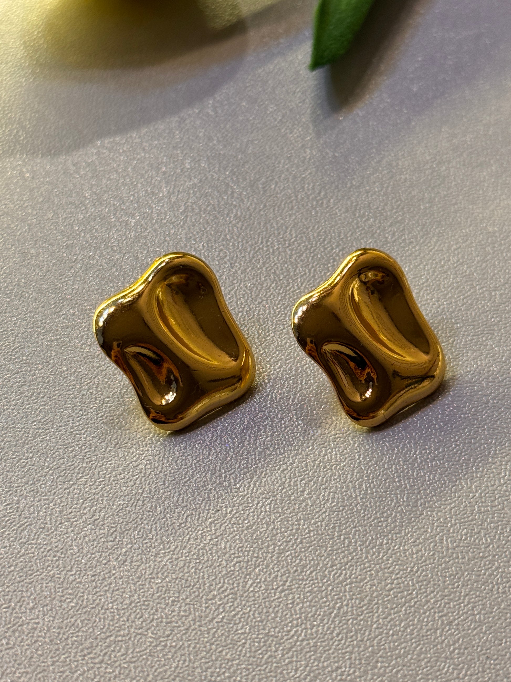 Two gold earrings on a light gray surface
