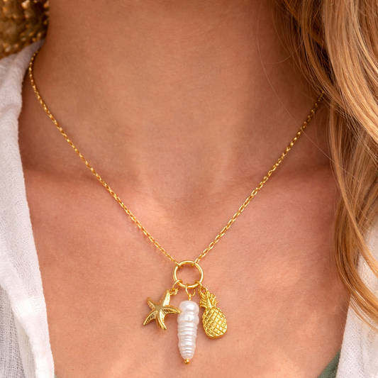 Gold necklace with starfish, shell, and pineapple charms on a person wearing a green top.