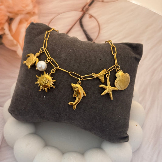 Gold bracelet with various charms on a gray jewelry cushion.