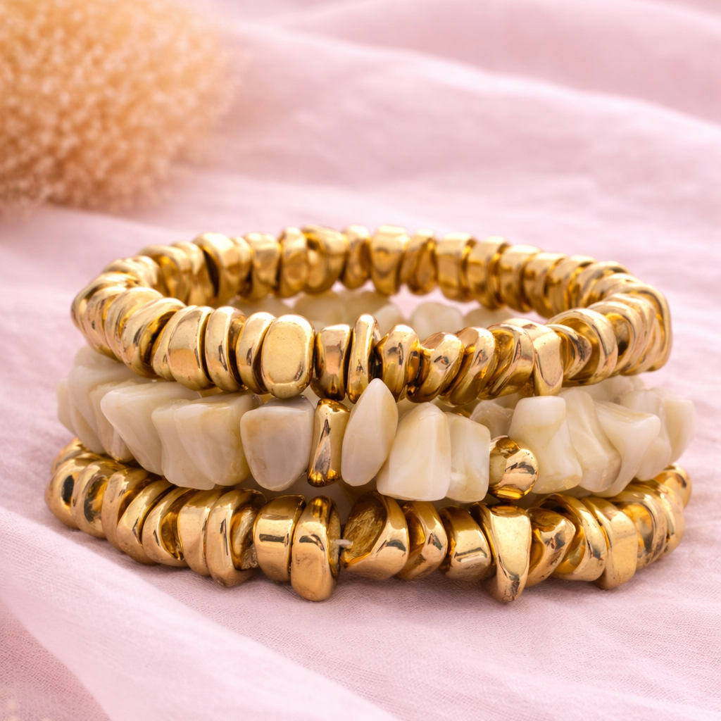 Stack of gold and beige beaded bracelets on a pink fabric background
