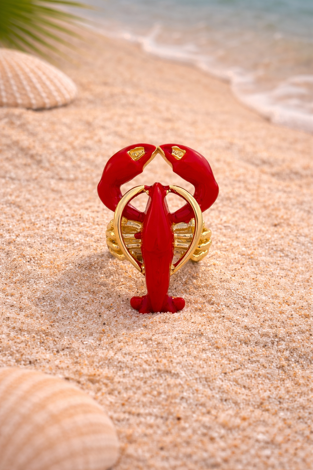 Red and gold lobster-shaped object on a sandy beach with shells and water in the background