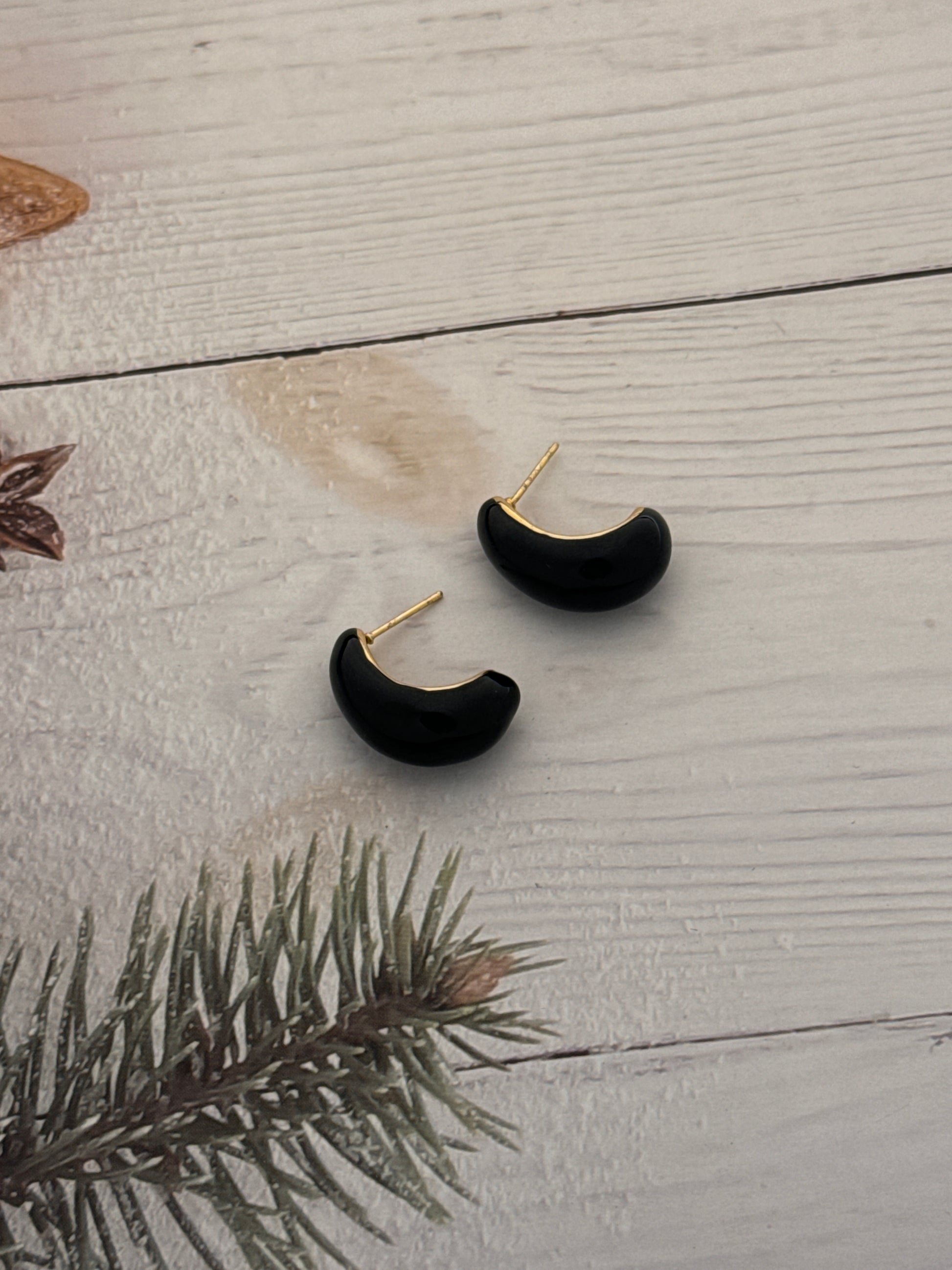 Black earrings with gold accents on a wooden surface with a branch.