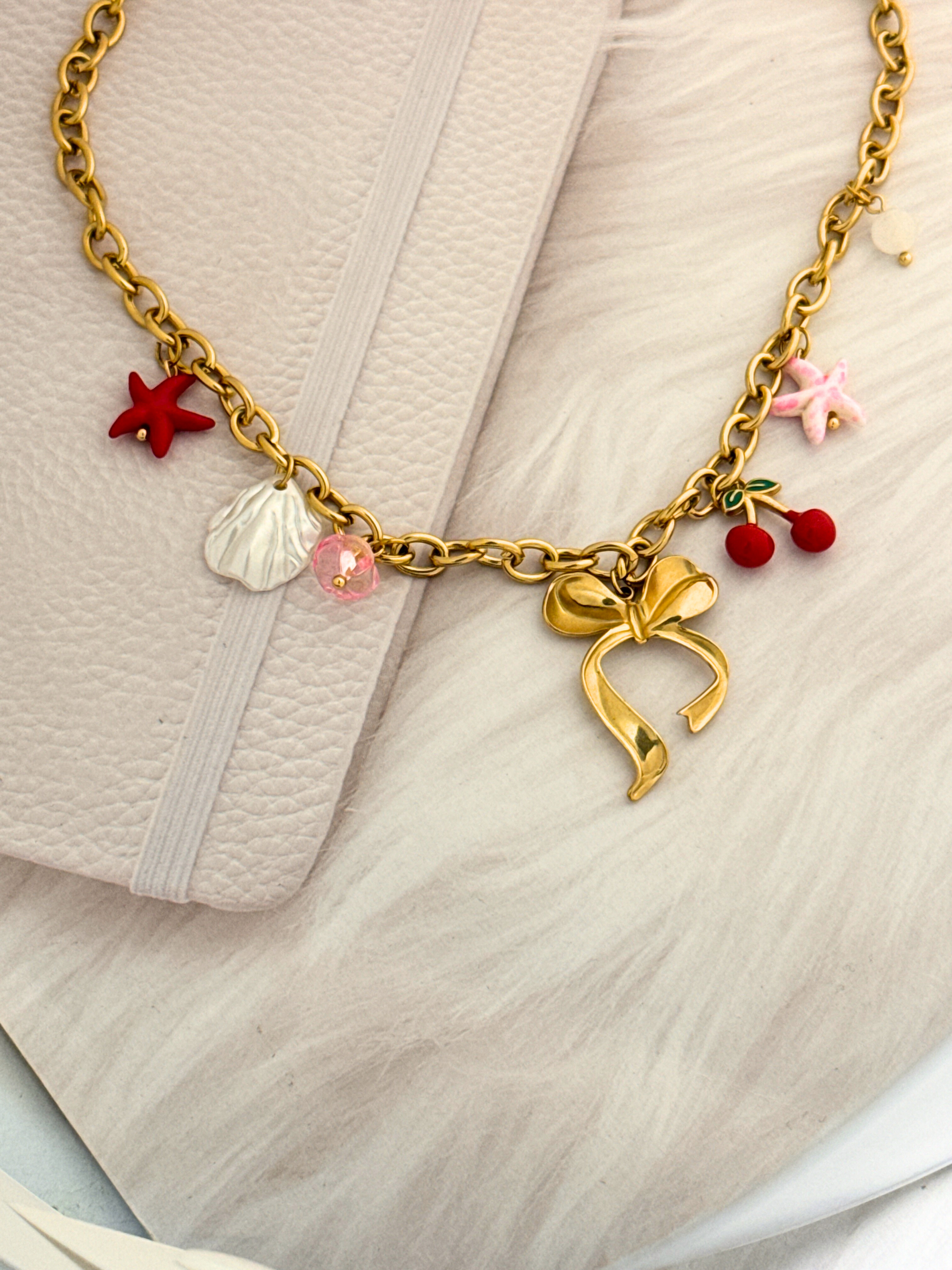 Gold necklace with bow charm and colorful charms on a light fabric background