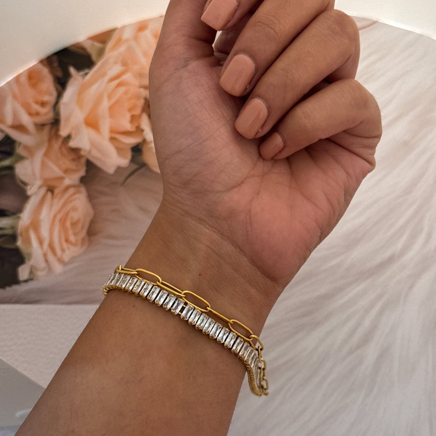 Hand wearing a gold bracelet with a blurred background of flowers