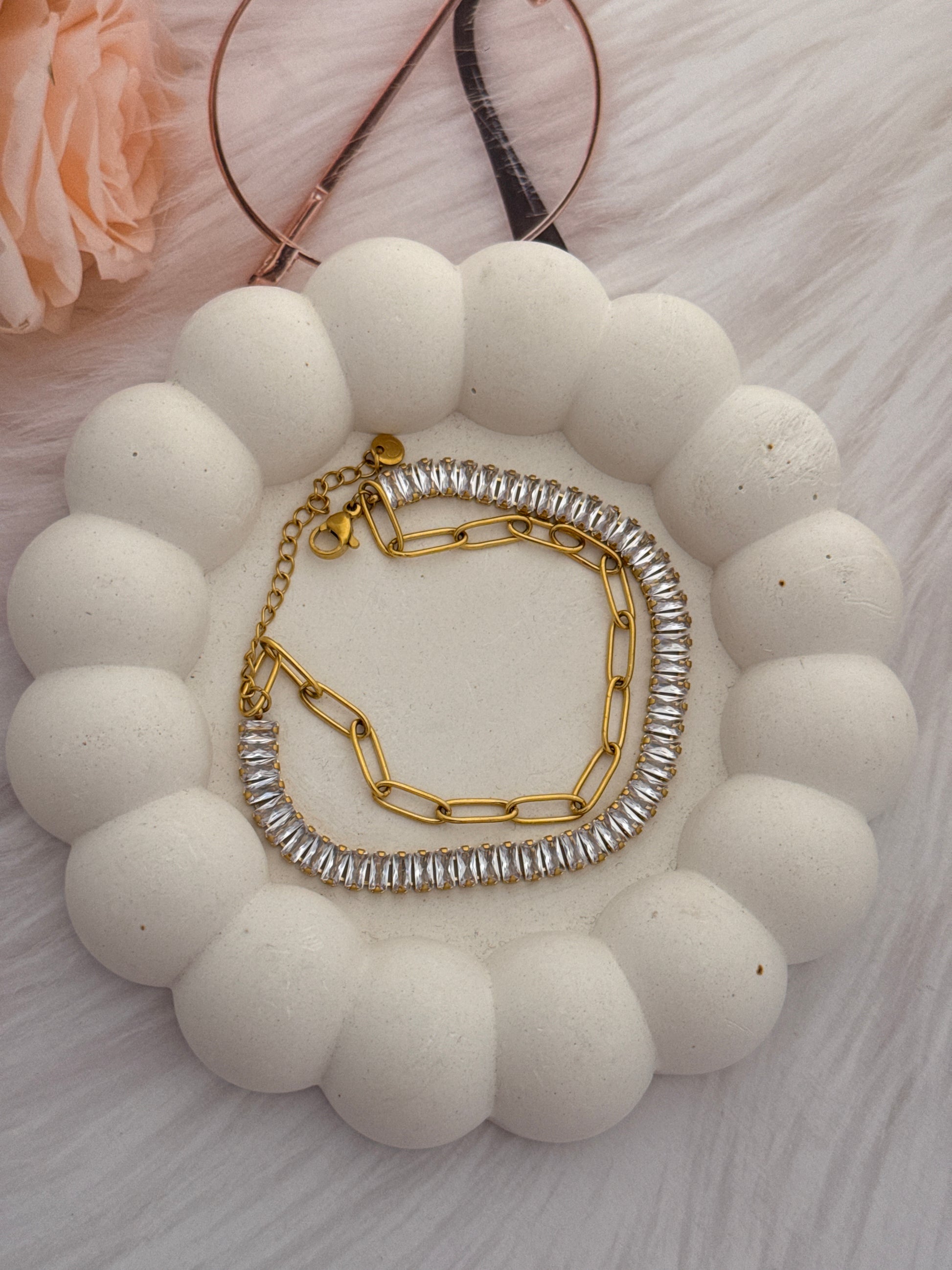 Gold and silver chain necklaces on a white spherical surface with a blurred flower in the background